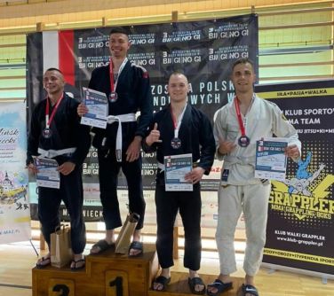 czterech uśmiechniętych mężczyzn z medalami i dyplomami stoi na podium