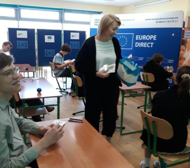 kobieta między ławkami uśmiecha się do jednego ucznia