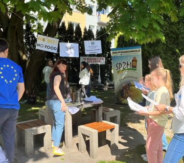 osoby na dworze trzymają kartki w dloniach rozmawiają