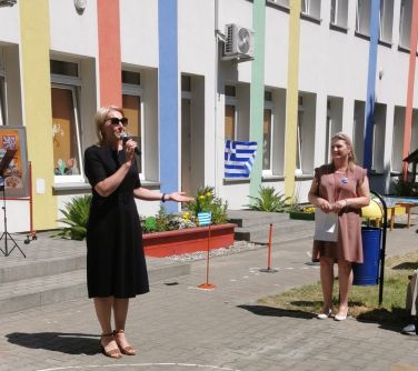 kobieta przemawia na dziedzińcu przed budynkiem obok osoby słuchające