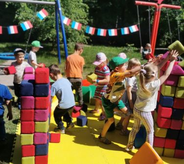dzieci bawią się na żółtej macie uykładają kwadratowe miękkie klocki