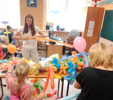 na stole długie balony, przed stołem pani skręca balony