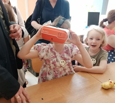 dwie dziewczynki siedzą w ławce szkolnej, jedna ma na głowei okulary VR