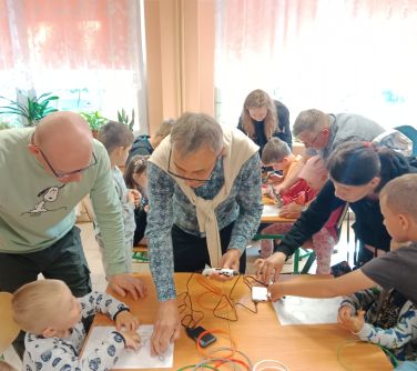 osoby pochyalają się nad ławką szkolną na której leżą skręcone kable