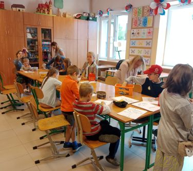 osoby siedzą naokoło złączonych ławek szkolnych