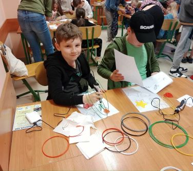 dzieci siedzą przy łakwach szkolnych układają coś ze skręconych kabli
