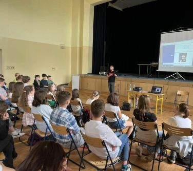 publiczność siedzi na krzesłach osoba przed nimi przemawia