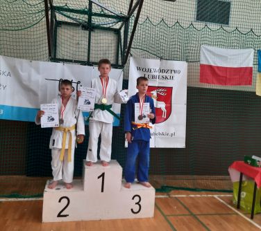 chłopcy pozują do zdjęcia stojąc na podium, trzymają dyplomy w dłoniach