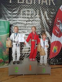 trzy dziewczynki pozuja na podium, trzymają w dłoniach dyplomy i torby papierowe, na szyjach medale