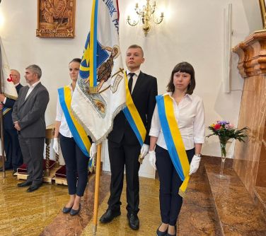 wnętrze kościoła, trzy osoby stoją ze sztandarem