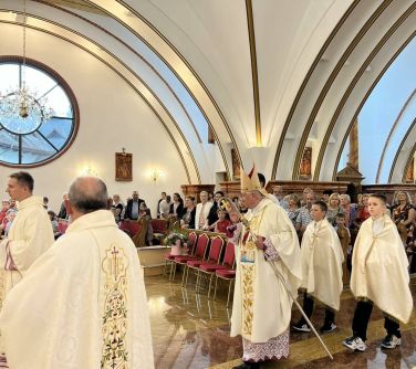 wnętrze kościoła, osoby siedzą w ławkach, środkiem idzie biskup za nim dwóch chłopców