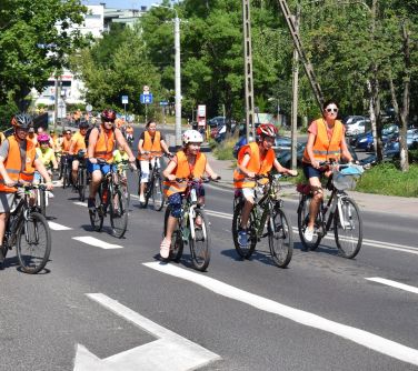 uczestnicu rajdu rowerowego w pomarańczowych kamilzekach jadą na rowerach jezdnią asfaltową przez miasto, na pierwszym...