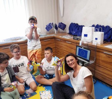 grupa dzieci i kobieta pozują do zdjęcia siedząc na piankowych matach