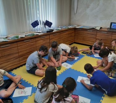 grupa dzieci siedzi na piankowych matach rysują