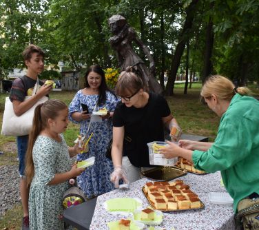 osoby zgromadzone pod pomnikiem Anny Mińskiej, przy stoliku dziewczynka odbierająca ciasto