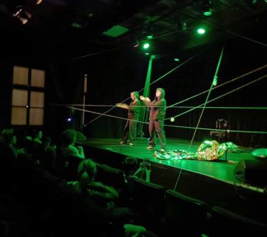 dwie kobiety stoja na scenie wśród nich rozwieszone sznurki, na scenie krzesło i pled foliowy
