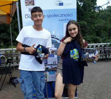 chłopiec i dziewczynka pozują do zdjecia na tle rollup'a, trzymają w rekach czarne koszulki