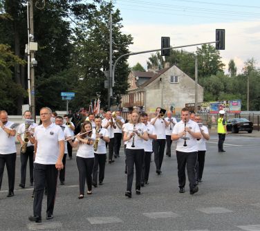 orkiestra w białych koszulkach przechodzi przez jezdnię grając