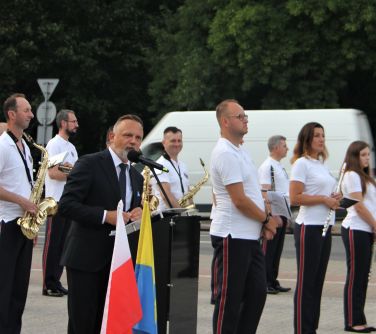 Burmistrz stoi przy mównicy i wygłasza przemówienie, w tle orkiestra dęta