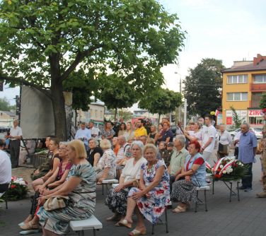 mieszkańcy miasta siedzą na ławkach i słuchają przemówień