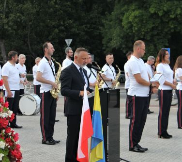 Burmistrz stoi przy mównicy i wygłasza przemówienie, w tle orkiestra dęta