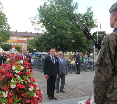 trzech mężczyzn - reprezentacja samorządów stoi przy pomniku niepodległości