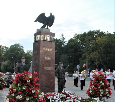 widok na posterunek honorowy, który stoi pod pomikiem niepodległosci ze złożonymi wieńcami i kwiatami