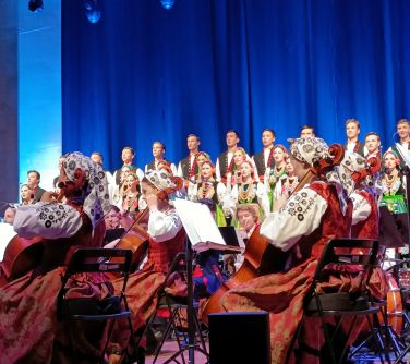 na scenie z tyłu chór śpiewa na przodzie orkiestra bokiem siedzi na krzesłach grają na instrumentach