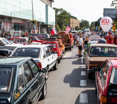 zabytkowe pojazdy stoją na ulicy, pomiędzy nimi osoby oglądające, po bokach budynki, z przodu duży dmuchany balon