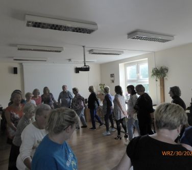 grupa osób w kółku trzymają się za ręcę, poruszają się w takt muzyki poruszając się na około