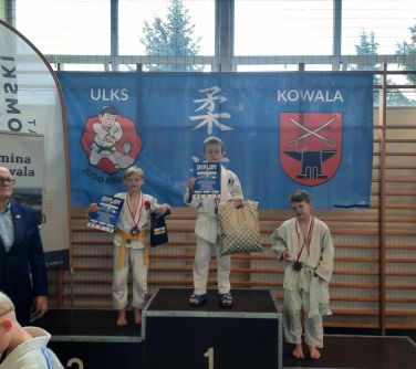 trójka chłopców pozuje na podium, dwóch z nich trzyma siatki i dyplomy w dłoniach, trzeci tylko siatkę, po lewej stronie...