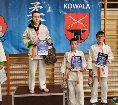 czterech chłopców stoi na podium trzymają dyplomy w dłoniach, na szyi medale, obok po prawej stronie jeden chłopiec trzyma...
