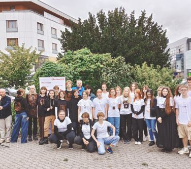 grupa osób pozuje do zdjęcia, w tle drzewa i budynki