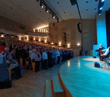 sala koncertowa, na scenie po lewej stronie artystka i jeden członek zespołu gra na akordeonie, po lewej stronie...