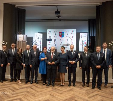 osoby pozują do zdjęcia, w tle podwyższona scena na któej stoja mikrofony, mównica, w tle banery