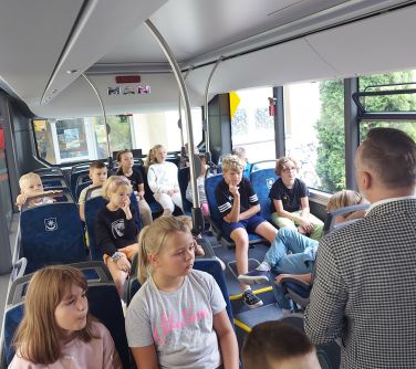 dzieci siedzą na siedzeniach w autobusie, przed nimi mężczyzna