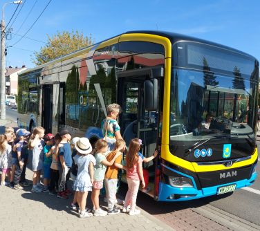 grupa dzieci na przodzie z kobietą wsiadają do autobusu