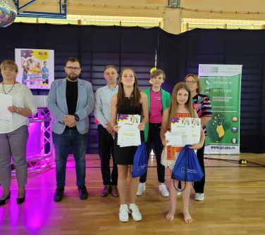 dwie laureatki konkursu pozują do zdjecia z dyplomami w ręku, za nimi stoi kilka dorosłych osób