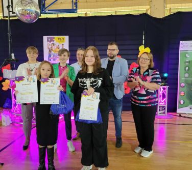 dwie laureatki konkursu pozują do zdjecia z dyplomami w ręku, za nimi stoi kilka dorosłych osób