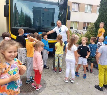 grupa dzieci ogląda zeroemisyjny autobus stojacy przed szkołą