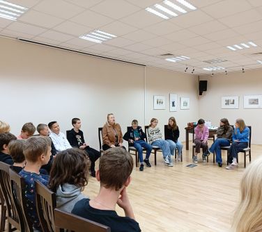 nastolatki wraz z prowadzącą kobieta siedzą w kole na krzesłach