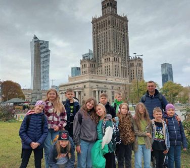 grupa dzieci ze szkoły podstawowej pozuje do zdjęcia, w tle pałac kultury i nauk/zdjęcie otwiera się w nowej karcie