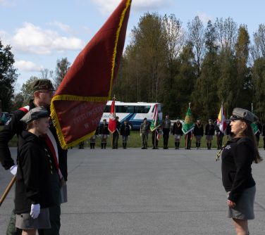 płyta lotniska, po prawej kobieta salutuje przed sztandarem, po lewej dwie kobiety i mężczyzna trzymający sztandar, w tle...
