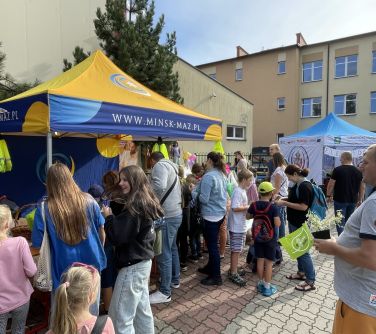 teren szkoły, grupa osób stoi naokoło namiotu, w tle budynek szkoły