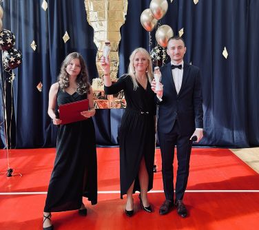 trzy osoby pozują do zdjęcia od prawej mężczyzna i kobieta trzymają w dłoniach zrobione oscary, w tle duży zrobiony oscar,...