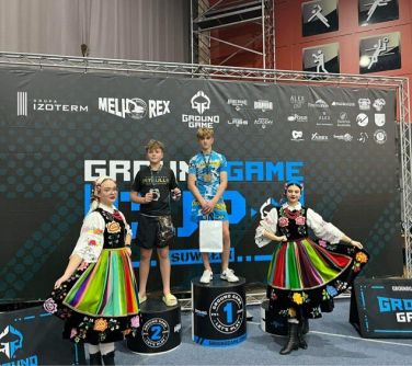 dwóch nastolatków na podium, po obu stronach kobiety ubrane w stroje ludowe, w tle baner