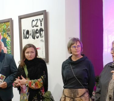 cztery osoby na tle ściany na której wisa dwa obrazy