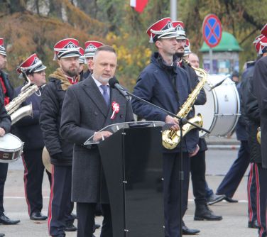 burmistrz przemawia stojąc przy mównicy,w tle stoi kilka osób z orkiestry