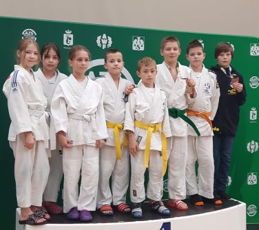 grupa dzieci w kimonach do judo pozuje do zdjęcia stojąc grupą na podium