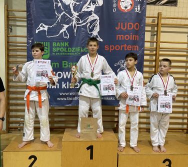 czterech chłopców pozuje do zdjęcia w kimonach judo, stoja na podium, w rękach trzymają dyplomy, na szyi medale. Chłopiec...